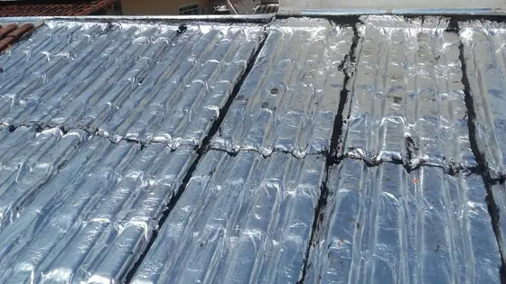 Telhado de telhas onduladas coberto por faixas de manta aluminizada, visto de perto