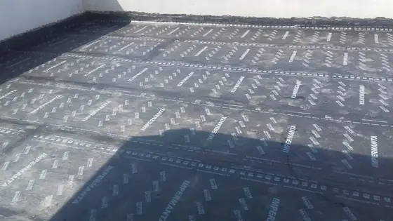 Laje grande inteiramente coberta de manta asfáltica, com as emendas das faixas e a estampa do fabricante visíveis