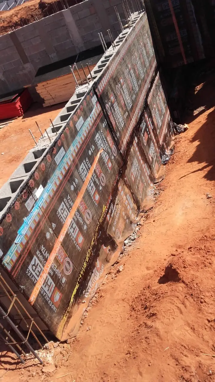 Muro de blocos de concreto com a manta asfáltica aplicada na face voltada para a terra, vista de cima, com barro vermelho ao lado