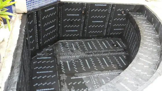 Piscina de canto curvo revestida de manta asfáltica preta estampada, com pastilha azul na borda de cima