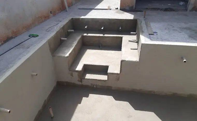 Piscina de concreto com banco e degraus, com as tubulações à mostra, antes do revestimento